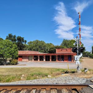 red brick building with brick columns and parking lot beside railroad tracks