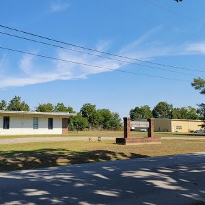 Single story white brick school building next to yellow corrugated metal building