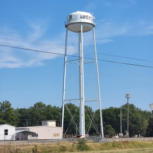 Large white metal water tower on legs with "Wheatley" on the side of tower and trees in background