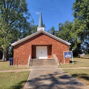 Single story red brick church building with steeple with cross on top