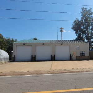 tan metal building with three garage bay doors next to a Quonset hut