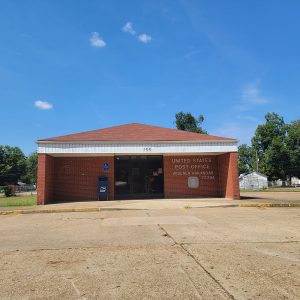 Single story red brick post office building with parking lot