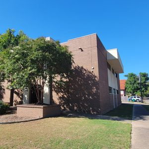 Multistory red brick building with trees and sidewalk