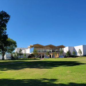 Multistory modern white building with walls of windows around the top floor with large lawn