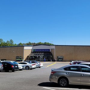 Single story brown concrete building with parking lot filled with cars