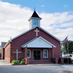 red brick church building with small white tower and parking lot