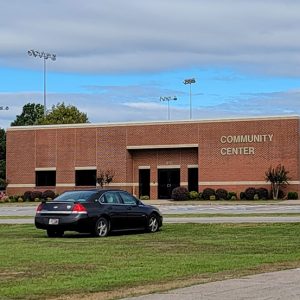 Multistory red brick community center building with parking lot and one car parked in the grass