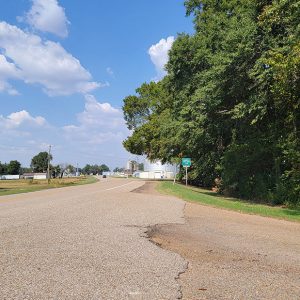 curved road with small buildings and large silos in the distance and trees in foreground