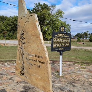 Large stone slab with painting of soldier beside a metal sign both planted in a stone foundation