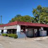 Single story gray and white concrete block building with red roof and parking lot