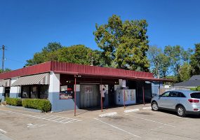 Single story gray and white concrete block building with red roof and parking lot