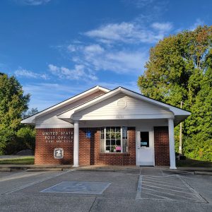 Single story red brick post office building with parking lot and flagpole