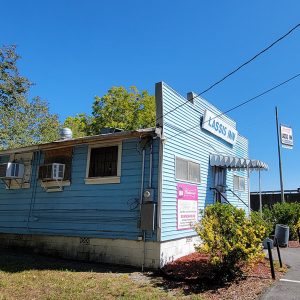 Single story blue wooden building with white awning over front entrance