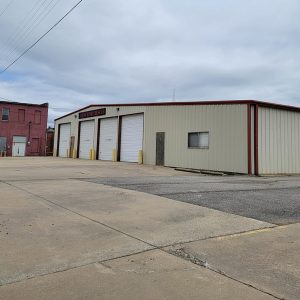 Single story beige metal building with four white bay doors and large paved lot