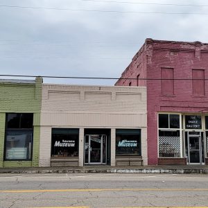 Single story beige brick building in row of storefronts with "Lavaca Museum" written on both front windows