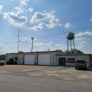 beige metal buildings with two central garage doors and water tower in background