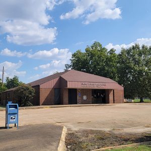 Single story red brick post office building with parking lot