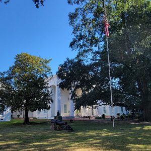 White multistory building with main section and branches and Greek columns and trees and a cannon