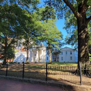 White multistory building with Greek columns and trees and black metal fence in front