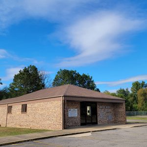 Single story blond brick post office building with flagpole flying American and P.O.W. flags