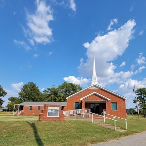 Single story red brick church building with white steeple