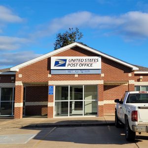 Single story red brick post office building with parking lot