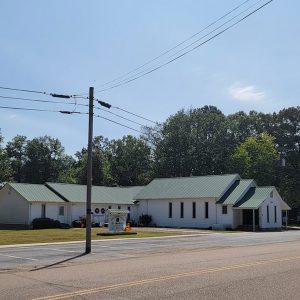 white church building with green roof and parking lot