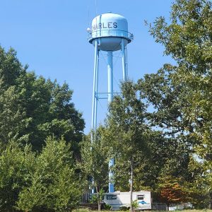 metal water tank on tall legs with trees in foreground and mobile home underneath