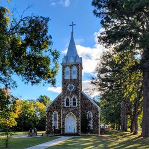 Multistory ornate stone church building with spire surrounded by trees