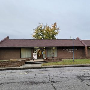 Single story brown brick library building with parking lot