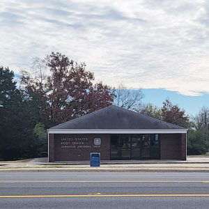 Single story red brick post office building with flagpole and trees in background