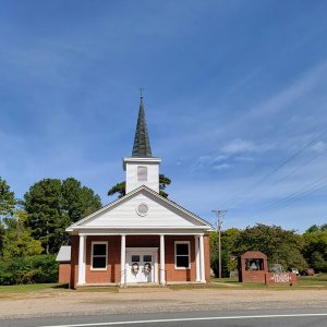 Single story red brick church building with covered entrance and steeple