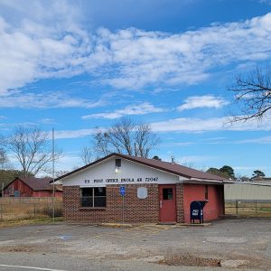 Single story red brick post office building with parking lot