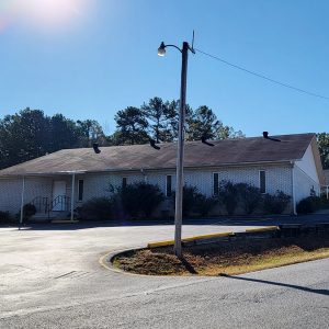 Single story white brick church building with stairs leading to entrance and parking lot