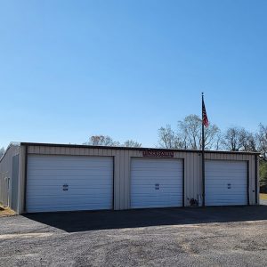 Single story white metal building with three garage doors