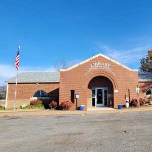 Single story red brick library building with covered entrance and parking lot