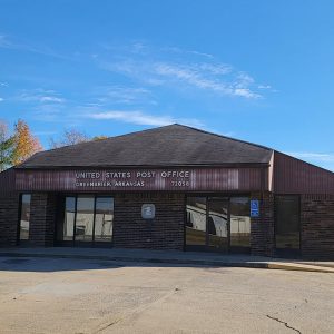 Single story brown brick post office building with parking lot