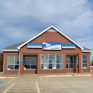 Single story red brick post office building with parking lot