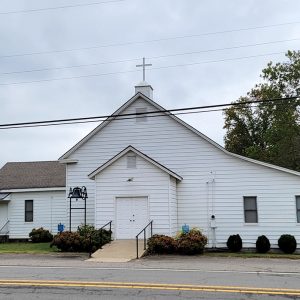 Multistory white wooden church building with a bell in front