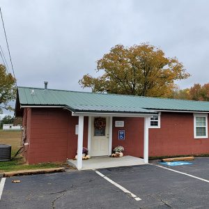 Single story red concrete block building with green roof and covered entrance and parking lot