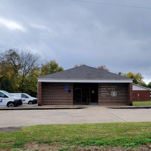 Single story red brick post office building with postal vehicles parked next to it