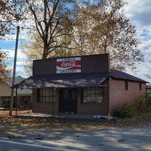 Single story red brick grocery store building with covered entrance and sign "Land's Grocery"