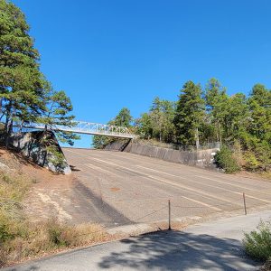 Concrete ramp with metal bridge over it and trees on both sides