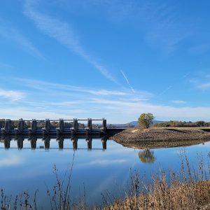 Large concrete and metal structure crossing a river with hills in the distance