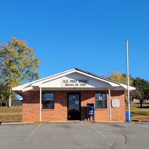 Single story orange brick post office building with parking lot