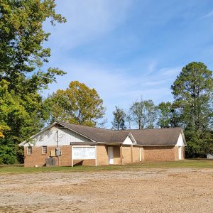 Single story orange brick church building with trees in background