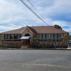 Single story rock building with covered walkway leading from it and parking lot