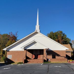 red brick church building with white steeple and parking lot