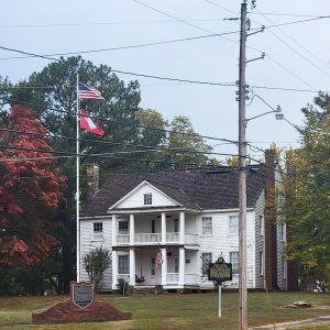 Multistory white wooden house with covered front porches on both levels and flagpoles in front