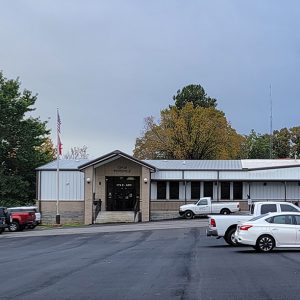 Single story white metal and blond brick building with cars parked out front